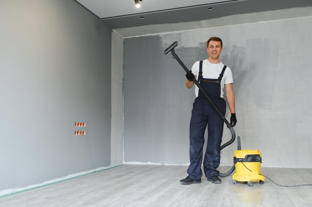 male worker in overall vacuum cleaning during apartment renovation